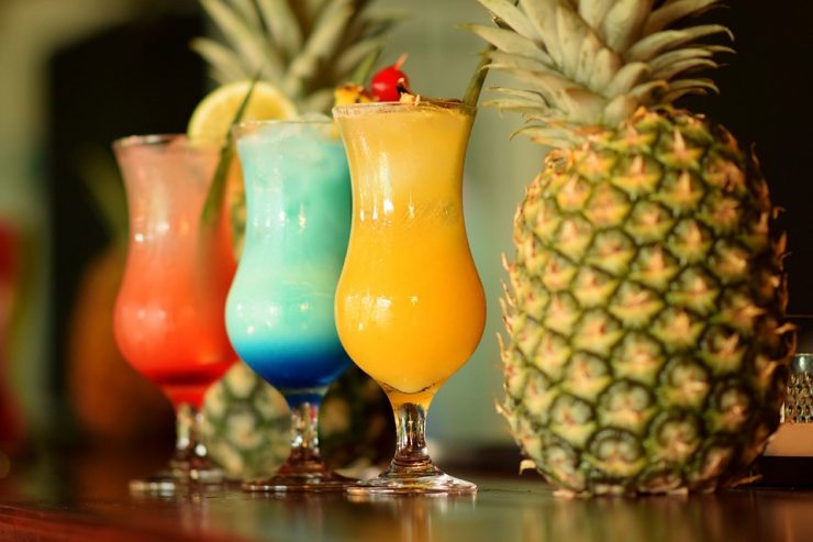 três drinks de frutas com abacaxi ao fundo